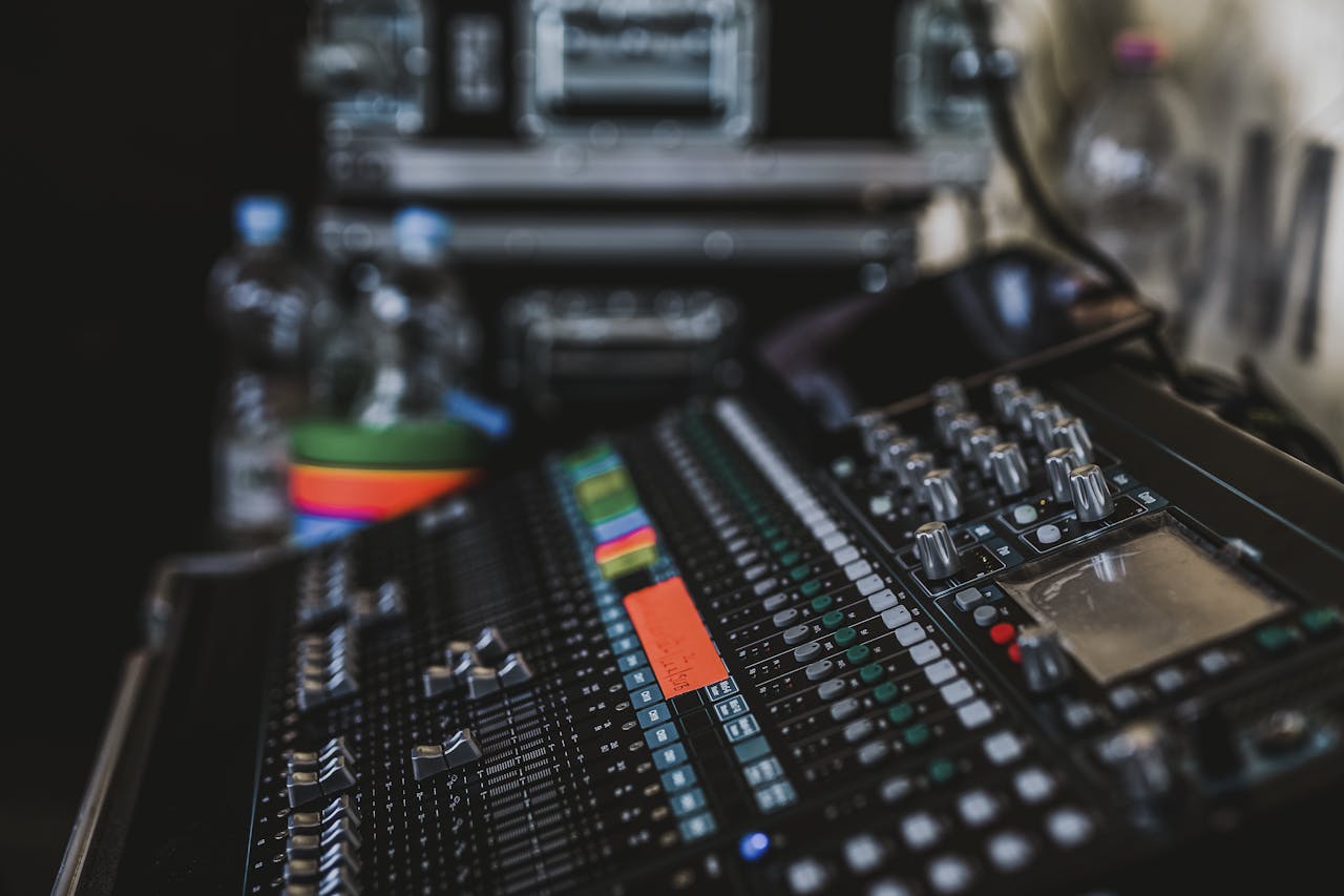 Close-up of a professional audio mixer with various knobs and sliders in a music studio setting.